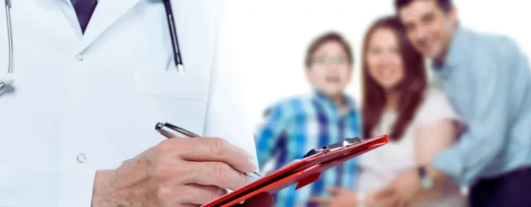 Lekarz notujący informacje na czerwonym klipbordzie, w tle uśmiechnięta rodzina – kobieta w ciąży, mężczyzna i dziecko. Obraz symbolizuje troskę o zdrowie i wsparcie dla rodzin w potrzebie, w kontekście tematu: wykaz sprzętu rehabilitacyjnego refundowanego przez PFRON.